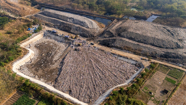 Aerial view of a large landfill site with heavy machinery and waste piles surrounded by agricultural fields in Klaten, Central Java, Indonesia.