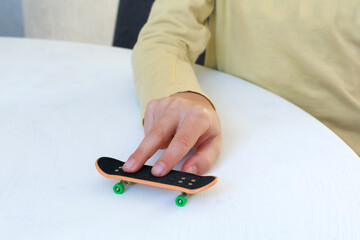 Hand controls a miniature fingerboard skateboard with two fingers on a white tabletop. Fingerboarding, hand coordination, balance, precision and recreational skill practice indoors. © Natallia