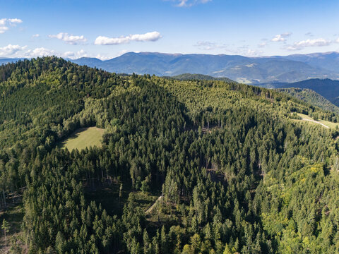 Aerial view of Vysoka mountain peak surrounded by dense coniferous forests, rolling hills, and a clear blue sky in the Slovak Ore Mountains, Lubietova, Banskobystricky kraj, Slovakia.