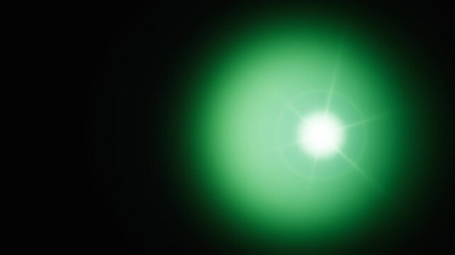 A bright glowing green light source with optical lens flare effect against black background