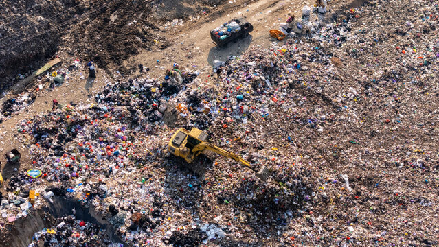 Aerial view of a large landfill site with a yellow excavator moving waste piles in Klaten, Central Java, Indonesia.