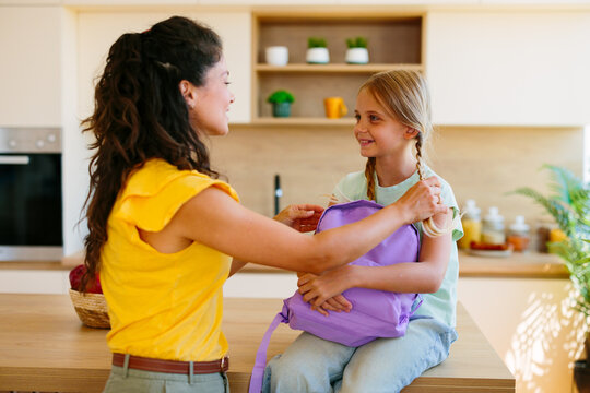 Mother helping daughter adjust her school backpack before leaving home