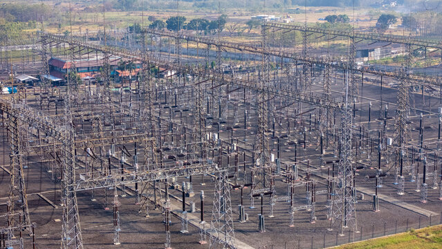 Aerial view of an electrical substation with high-voltage power lines, metal towers, and transformers set against a rural landscape in Klaten, Central Java, Indonesia.