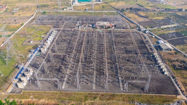 Aerial view of an electrical power substation with high-voltage transformers and transmission towers surrounded by rural fields in Klaten, Central Java, Indonesia.