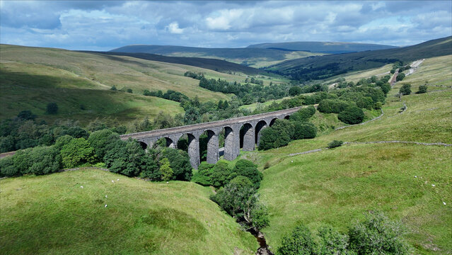 Aerial view of Dent Viaduct spanning the lush green valley with rolling hills and stone arches in Yorkshire Dales, North Yorkshire, UK.