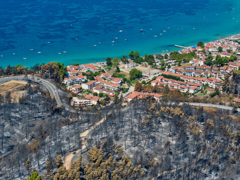 Siviri, Greece - 18 August 2026: Aerial view of the coastal town of Siviri showing the aftermath of a wildfire with burnt forest areas adjacent to the residential buildings and the turquoise sea.
