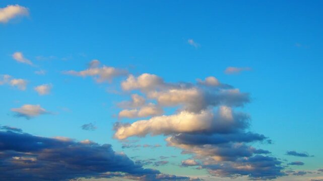 View clouds as they move slowly across a clear blue sky in an open area over the course of the day. The changing light alters the appearance of the clouds