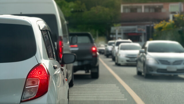 Rear view of white car turn on brake light because the car in front braked. Cars were driving in a long line on the asphalt road. Vehicles were passing by on the opposite side. with town and trees.