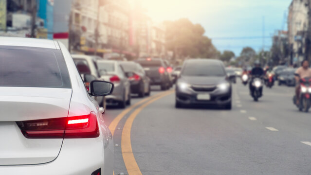 Rear side of car with tun on brake light on asphalt road. Cars navigate through a busy city street during daytime traffic congestion. Cars were parked in a long queue. 