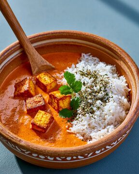Paneer curry with white basmati rice, grilled cheese cubes and fresh cilantro served in rustic bowl with wooden spoon