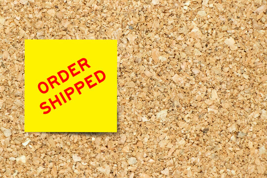 Yellow note paper with word order shipped on cork board background with copy space