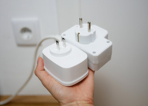 Two types of socket plugs - European round-pin plug and American flat-pin plug. Universal travel adapter in a hand close up. Electric plug adapter, international plug socket gadget for travel.