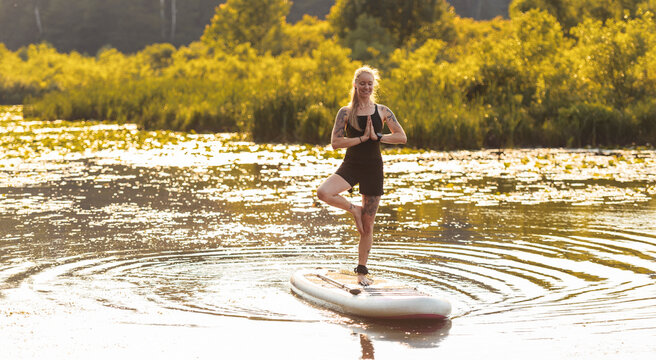 woman paddleboarding on calm waters doing yoga on sunset
