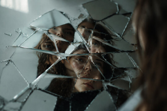 Shattered mirror reflecting fragmented facial features with soft window lighting.