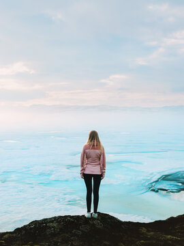 Female traveler walking at snowy frozen lake in Norway mountains, tourist woman on winter vacation enjoying outdoor adventure freedom solitude and connection with nature minimal scenery