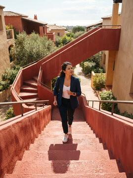 Woman in a navy blazer climbing wide reddish brown concrete outdoor stairs