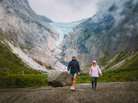 Couple hiking with Briksdalsbreen glacier view in Norway, man and woman tourists group travel together enjoying romantic vacations in mountains friends on adventure trip family lifestyle eco tourism