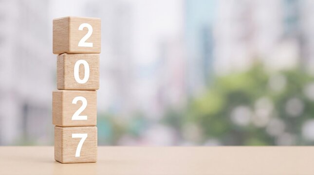 Four stacked wooden blocks displaying the year 2027 on a wooden surface outdoors