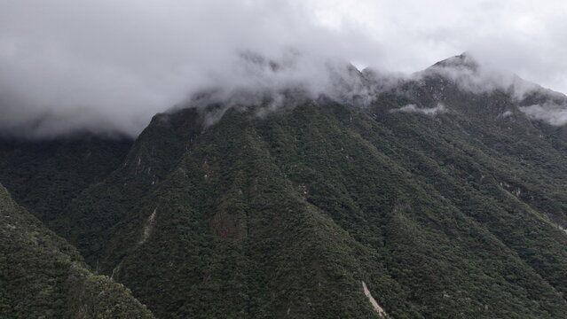 Aerial view of the lush, steep mountains partially obscured by low-hanging clouds and mist, showcasing the rugged Andean landscape in Aguas Calientes, Cuzco, Peru.