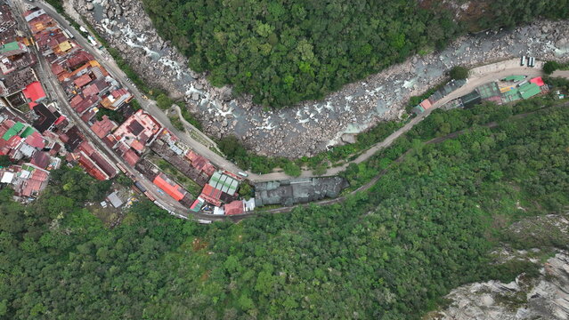 Aerial view of Aguas Calientes town nestled along the Urubamba River, featuring colorful rooftops, dense surrounding jungle, and winding mountain roads in Aguas Calientes, Cuzco, Peru.