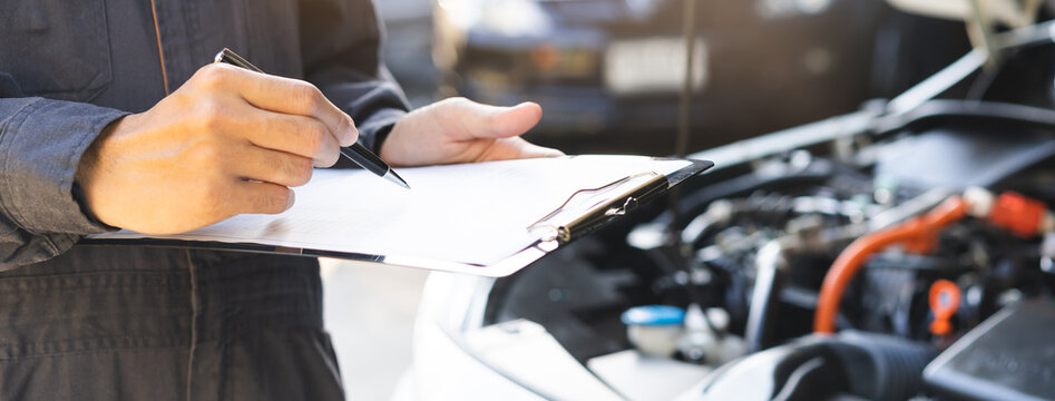 Auto check, car service shop concept. Automobile repairman writing job checklist on clipboard, mechanic checking engine to estimate repair machine, inspecting maintenance by engineer at vehicle garage