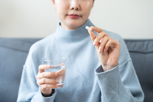 Sick, asian young woman, girl hand holding pill, painkiller medicine from stomach pain, headache, pain for treatment, take drug or vitamin and glass of water at home, pharmacy and health care concept.