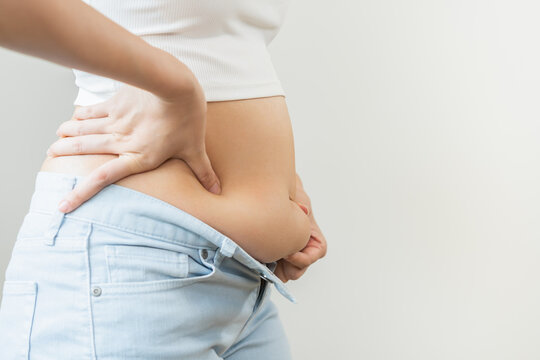Weight gain, overweight, high cholesterol and pressure, woman hand pinching excess fat big belly with finger and wear tight trousers, show fat around abdomen body, getting loss, isolated on background