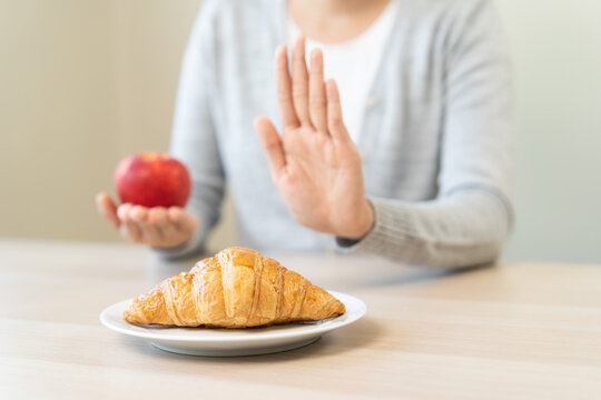 Ketogenic, Low carb, Intermittent Fasting Diet hand push out, refuse butter croissant bread on plate choose apple for good food, fighting to keep it from getting fat. Healthy nutrition of weight loss.
