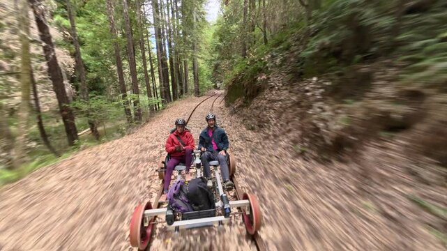 Mature couple enjoys riding an electric railbike over old railroad tracks in a forest of redwood trees near Fort Bragg, California.