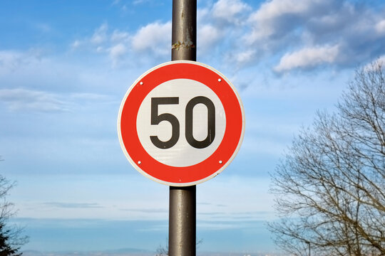 Red round 50km/h speed limit sign on highway in front of blue sky