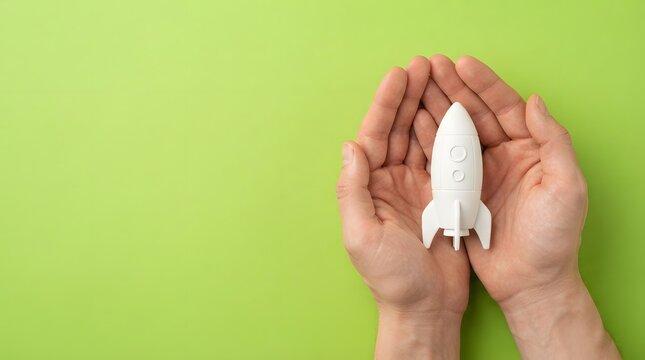 Hands holding a small white rocket ship model on a green background representing support and growth for the annual observance of world mental health day
