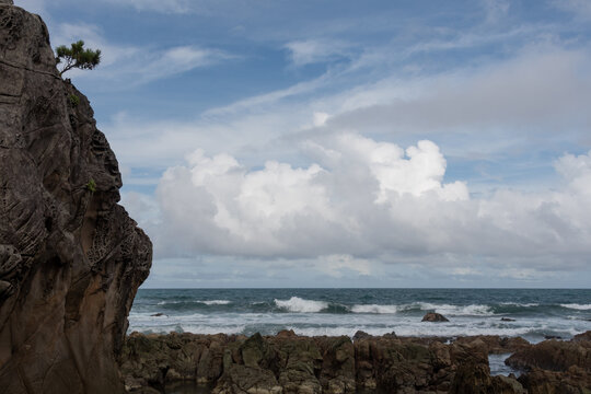 Rocky sea coast of Suzushima Island with dramatic summer clouds and waves under blue sky in Wakayama Japan