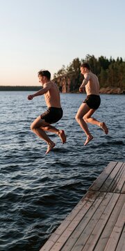 Two young men jumping off a wooden dock into a lake at sunset for summer adventure poster and background