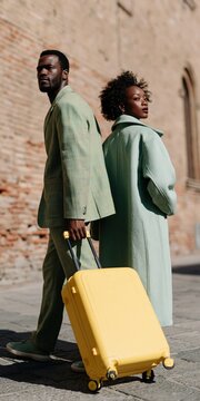 Stylish couple in coordinated mint coats walking with yellow suitcase on city street for travel fashion and urban lifestyle banner
