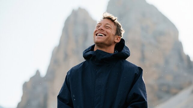 Laughing man in a navy rain jacket with rocky mountain background for outdoor lifestyle banner and social media header