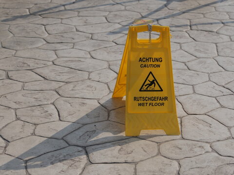 Bilingual caution slippery floor A-frame sign outdoors in sunlight