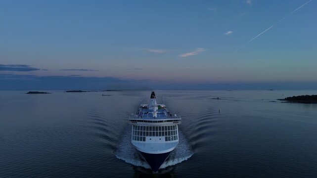 Aerial view of a passenger ferry sailing toward the camera across calm Baltic Sea waters with small rocky islands in the distance and clear blue sky at sunset