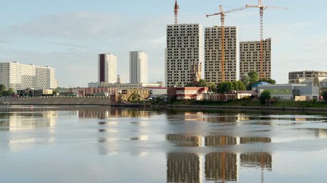 A city skyline rises behind the calm river. Construction cranes build a peaceful urban view. This lovely landscape highlights Saint Petersburg.
