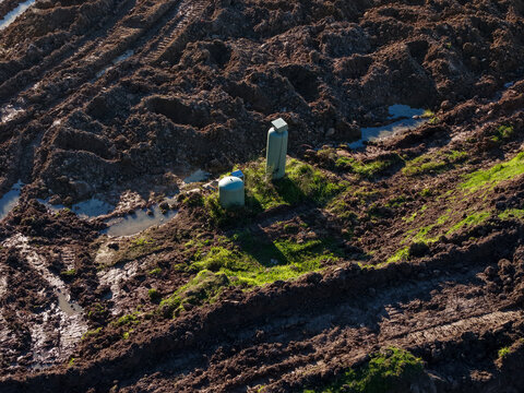 Aerial view of a muddy construction site featuring two industrial tanks on a small grassy patch surrounded by deep tire tracks and puddles in Kilsyth, Victoria, Australia.