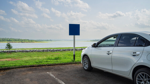 White car parked at outdoor parking lot near lake with blank blue sign