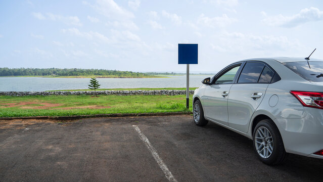 White car parked at outdoor parking lot near lake with blank blue sign