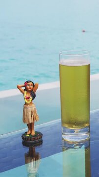 Beer. Glass of beer by hotel pool and hula dancer doll. Luxury resort travel vacation concept. Raw real unedited vertical video.