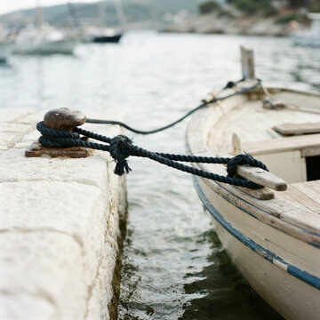 Small wooden boat tied to a stone dock with sailboats on calm grey water