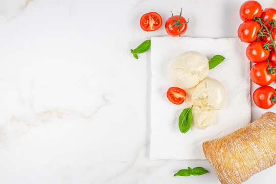 Fresh mozzarella cheese balls with cherry tomatoes and basil leaves on a white marble countertop, accompanied by a rustic loaf of bread. space for text