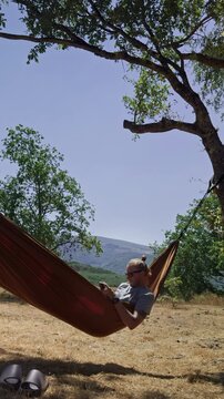 Young man relaxing in a hammock while using smartphone
Young man gently swinging in a hammock while browsing his smartphone surrounded by green mountains and trees. Modern outdoor lifestyle