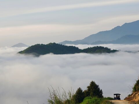 Small Off-Road Vehicle Driving Along Dirt Path Above Cloud Level in Mountains.