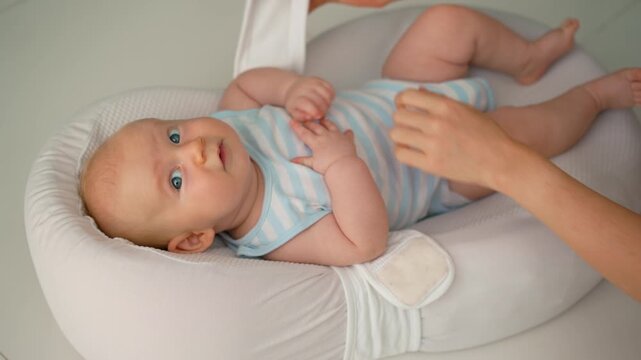 Mother placing baby in soft baby nest and fastening belt. Close-up.