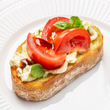 Fresh bruschetta topped with sliced tomatoes and basil on toasted bread served on a white plate with a textured rim, showcasing vibrant colors and appetizing presentation