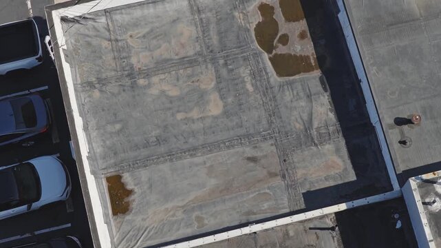 Aerial drone view above flat industrial retail business building rooftop and even roof with canvas having water damage from heavy rain and rainfall causing leaks and tears on roof's top with flooding