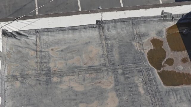 Aerial drone view above flat industrial retail business building rooftop and even roof with canvas having water damage from heavy rain and rainfall causing leaks and tears on roof's top with flooding